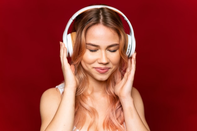 Chica adolescente con cabello rosado sobre fondo rojo aislado escuchando música