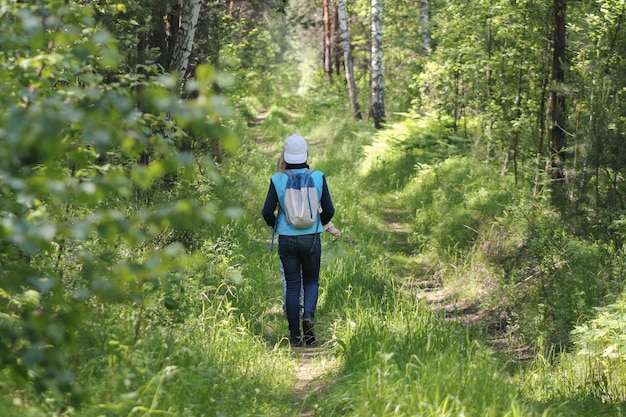 Chica adolescente caminando en el bosque en el día de verano, vista trasera, telefoto