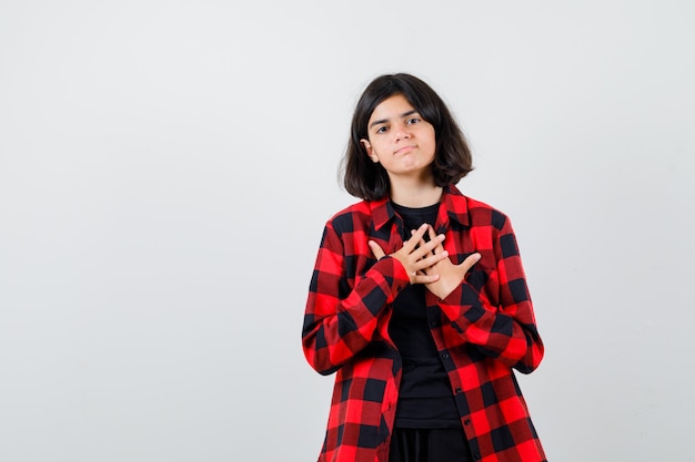 Chica adolescente en camisa casual cogidos de la mano en el pecho y mirando pensativo, vista frontal.