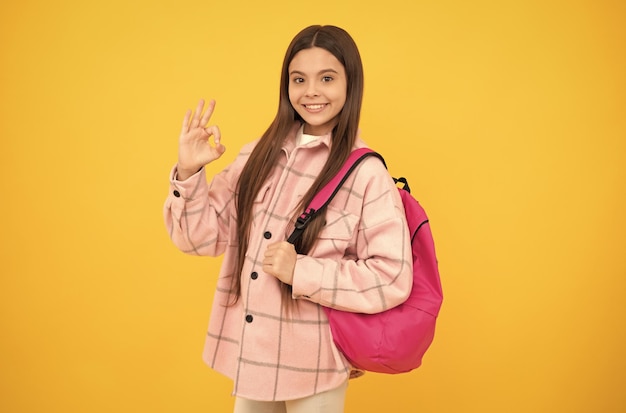 Chica adolescente en camisa a cuadros niño feliz estilo casual llevar mochila entre niño con mochila escolar infancia y educación estilo de moda de otoño estudiante alegre mostrar ok gesto de regreso a la escuela