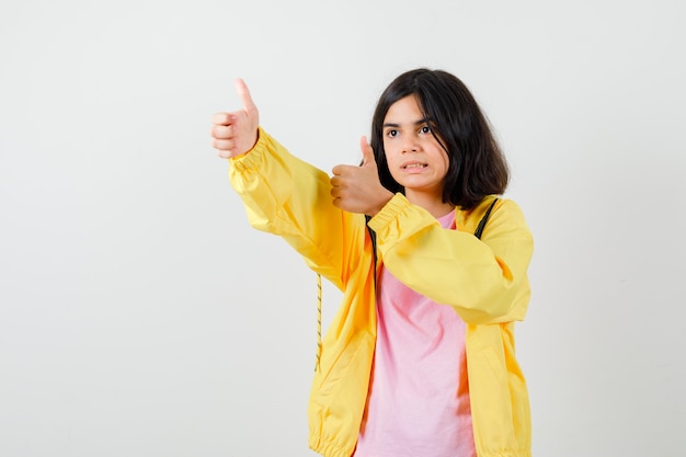 Chica adolescente en camiseta, chaqueta mostrando los pulgares hacia arriba y mirando complacido, vista frontal.