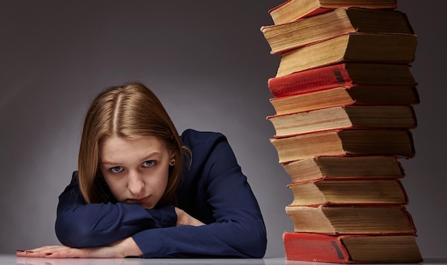 Chica adolescente cansada y aburrida molesta por el aprendizaje difícil mirando la pila de libros estresada por la preparación de la prueba de examen, estudiante abrumada exhausta con demasiada tarea de estudio, concepto de educación aburrido