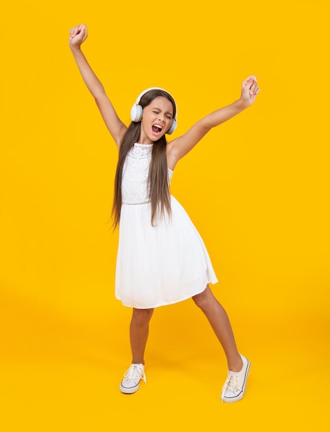 Chica adolescente cantando escuchar música en auriculares y bailar sobre fondo amarillo