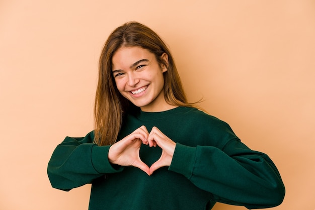 Chica adolescente caucásica flaca joven sonriendo y mostrando una forma de corazón con las manos.