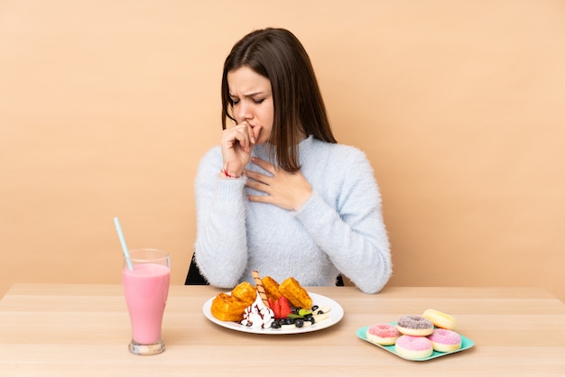 Chica adolescente comiendo gofres en beige sufre de tos y se siente mal