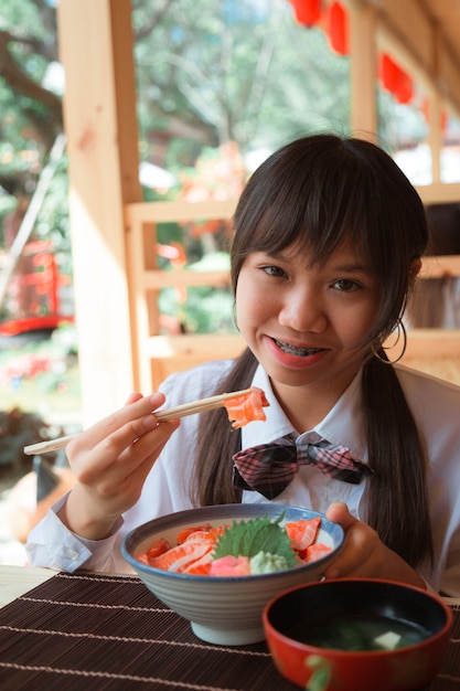 Una chica adolescente comiendo salmón don en un restaurante.