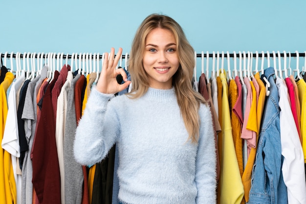 Chica adolescente comprando algo de ropa en la pared azul que muestra bien firmar con los dedos