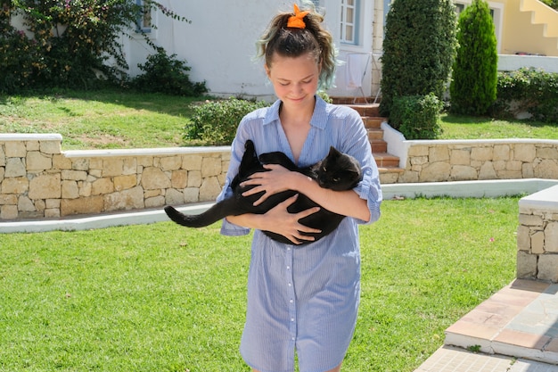 Chica adolescente corriendo con hermoso gato negro en sus brazos, día soleado de verano