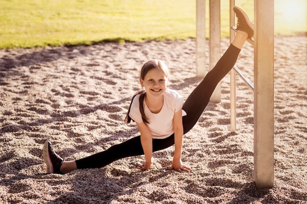 Chica adolescente divertida haciendo ejercicio de entrenamiento de divisiones al aire libre. Chica adolescente entrena Yoga afuera.