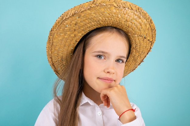 Chica adolescente con un elegante sombrero de paja sobre un fondo azul.