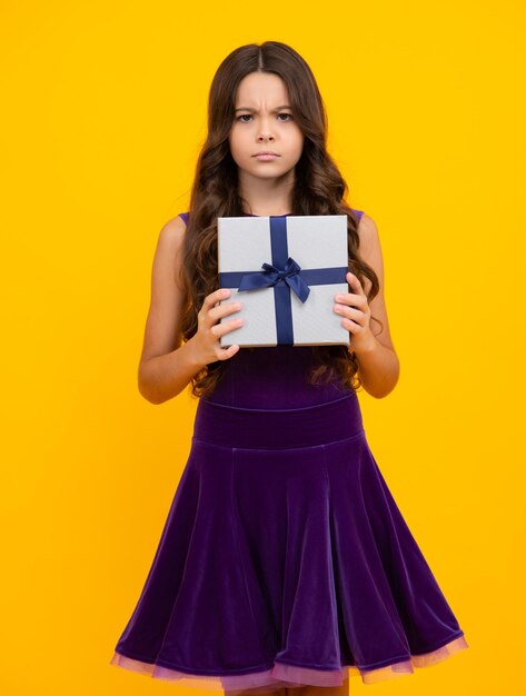 Chica adolescente enojada molesta e infeliz emoción negativa Niño adolescente sosteniendo caja de regalo sobre fondo amarillo aislado Regalo para niños cumpleaños Caja de regalo de Navidad o Año Nuevo