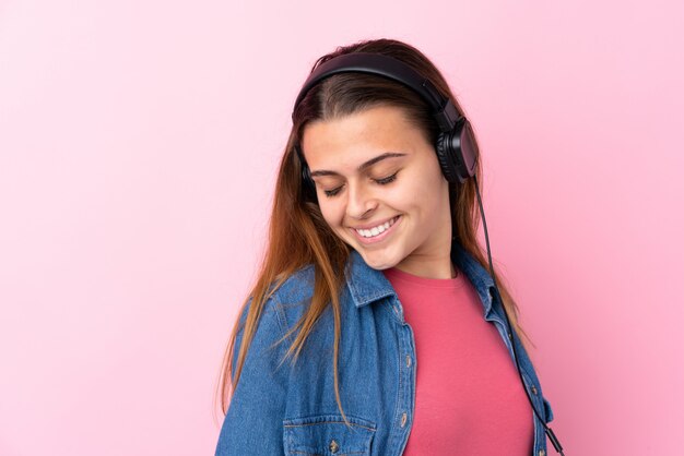 Chica adolescente escuchando música y bailando sobre pared rosa aislado