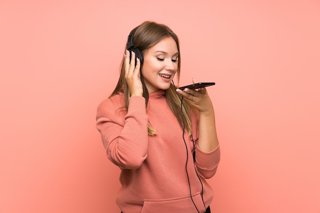 Chica adolescente escuchando música con un móvil sobre fondo rosa aislado