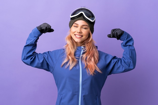 Chica adolescente esquiador con gafas de snowboard sobre púrpura aislado haciendo gesto fuerte