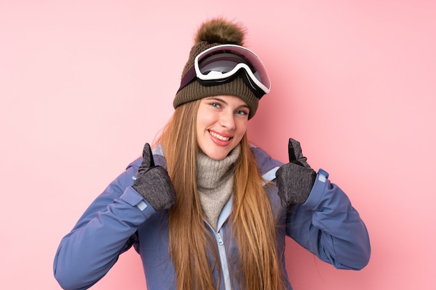 Chica adolescente esquiador con gafas de snowboard sobre rosa aislado dando un gesto de pulgares arriba