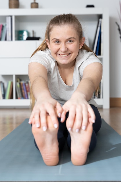 Chica adolescente estirando los músculos isquiotibiales Mujer rubia sosteniendo los pies con las manos