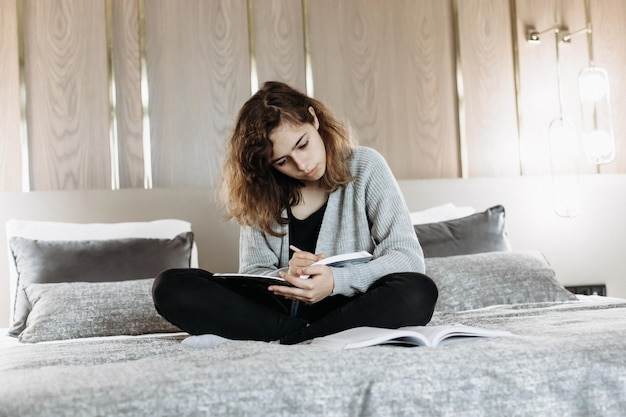 Chica adolescente estudiando en la cama en casa Estudiante haciendo la tarea