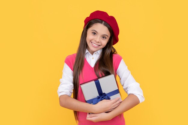 Chica adolescente feliz en boina francesa espera presente o caja de regalo en venta de fondo amarillo