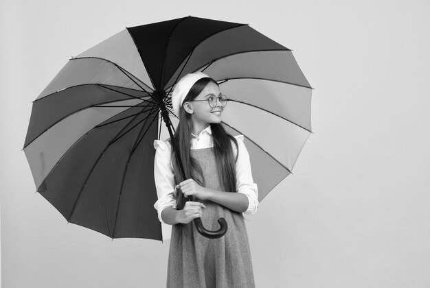 Chica adolescente feliz en boina bajo un paraguas colorido para protección contra la lluvia en la infancia de la temporada de otoño