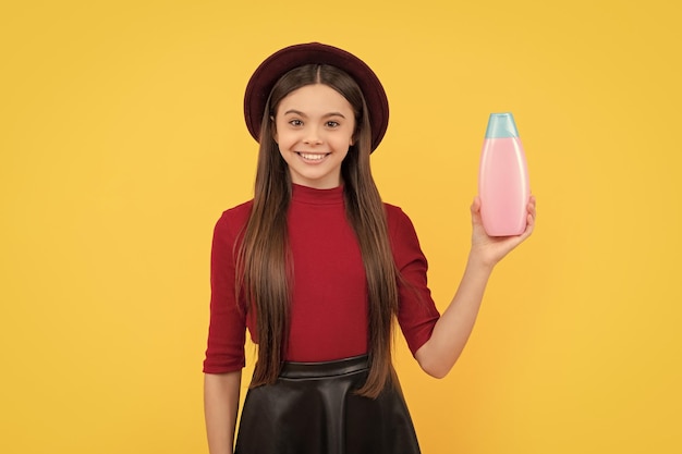 Chica adolescente feliz cabello largo con loción corporal sobre gel de ducha de fondo amarillo