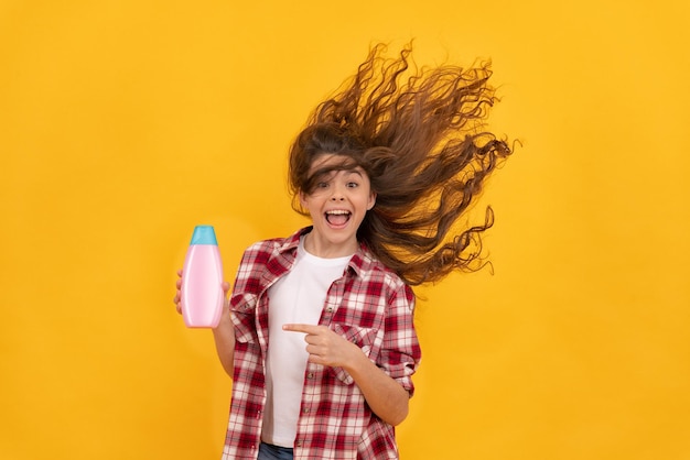 Chica adolescente feliz con cabello largo y rizado mantenga la belleza de la botella de champú