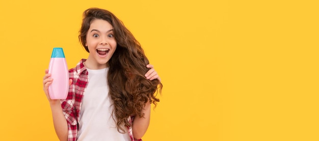 Chica adolescente feliz con cabello largo y rizado sostenga el volumen del cabello de la botella de champú
