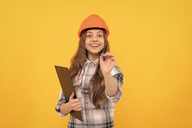 Chica adolescente feliz con casco y camisa a cuadros haciendo notas en la infancia del portapapeles