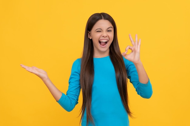 Chica adolescente feliz con gesto bien presentando producto sobre fondo amarillo con anuncio de espacio de copia
