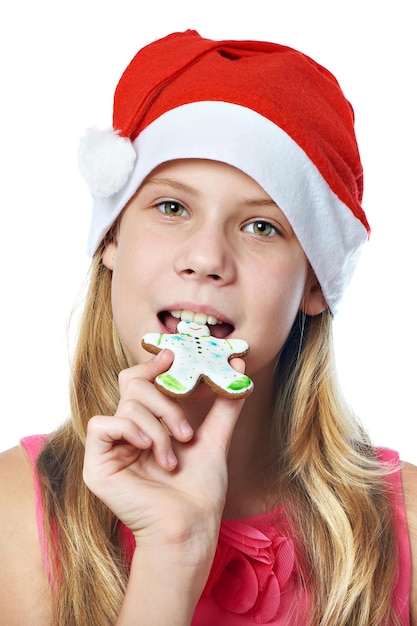 Chica adolescente feliz en gorra roja comiendo galleta de Navidad aislado