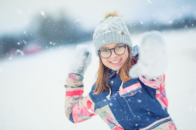 Chica adolescente feliz de invierno jugando en la nieve lanzando bolas de nieve.