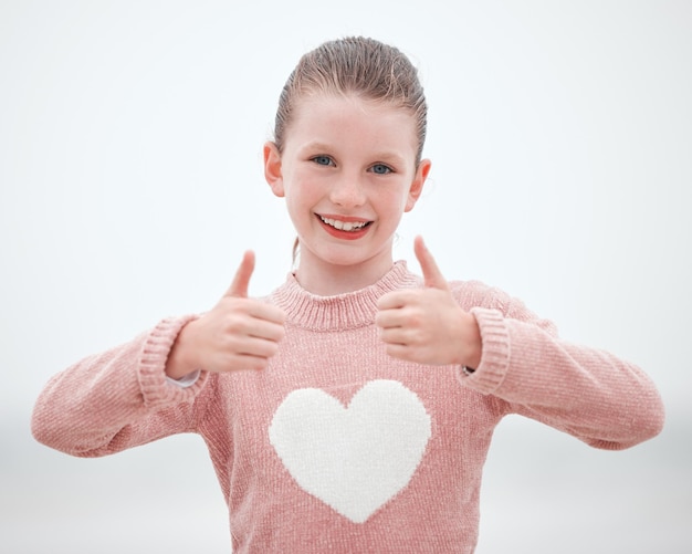 Chica adolescente feliz y las manos en los pulgares hacia arriba con una sonrisa para el signo o símbolo del gesto contra un fondo gris