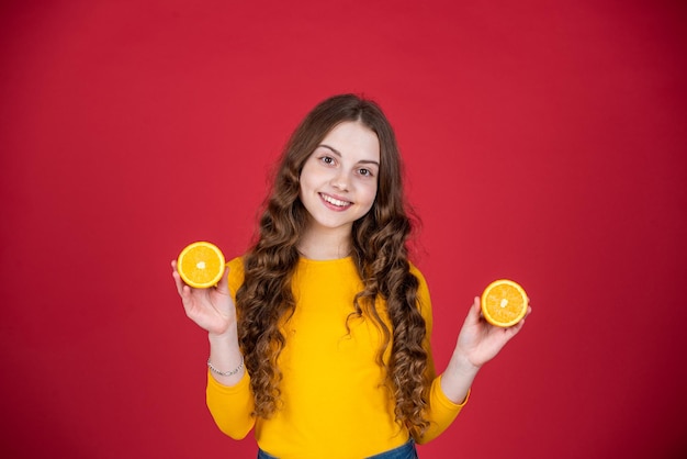 Chica adolescente feliz mantenga fruta naranja sobre fondo púrpura