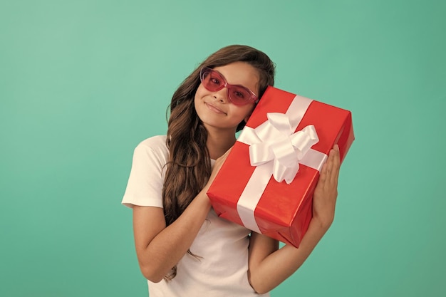 Chica adolescente feliz de moda en gafas de sol con saludo de ocasión de caja de regalo