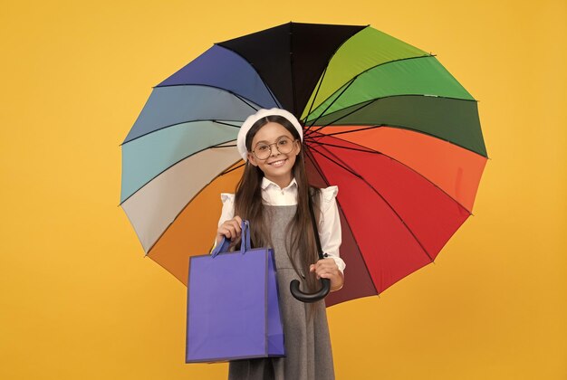 Chica adolescente feliz bajo un paraguas colorido en la temporada de otoño mantenga la bolsa de compras venta de otoño