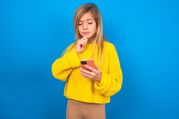 Chica adolescente feliz pensativa con suéter amarillo mantenga la mirada del teléfono revisando la notificación de las redes sociales