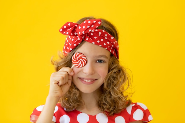 Chica adolescente feliz con piruleta roja contra la pared amarilla