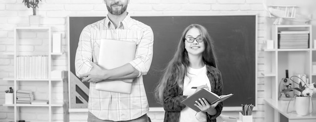 Chica adolescente feliz y profesor recortado en la escuela secundaria con libro de trabajo en el estudio de pizarra