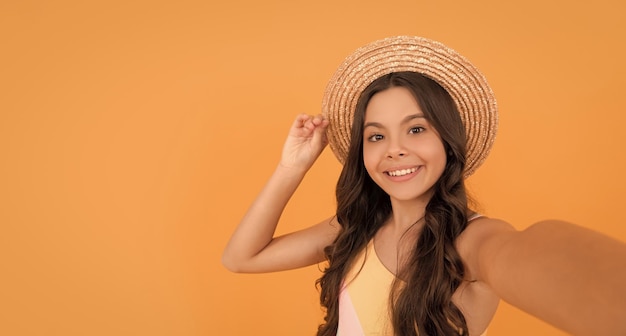 Chica adolescente feliz en sombrero de paja de verano haciendo selfie en espacio de copia de fondo naranja haciendo selfie