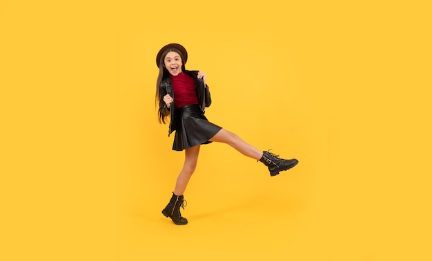 Chica adolescente feliz con sombrero y ropa de cuero dando un gran paso adelante, adelante