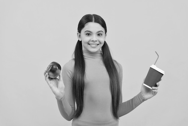 Chica adolescente feliz con taza de café para llevar y manzana en el almuerzo de fondo amarillo