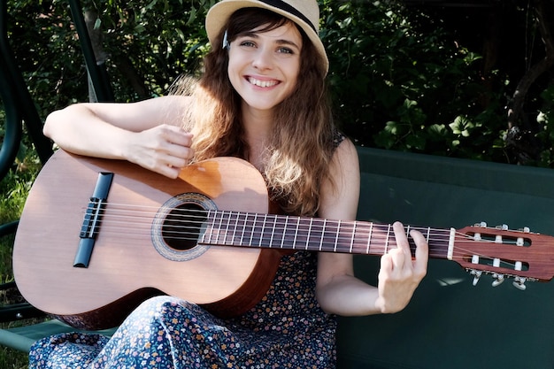 Chica adolescente feliz tocando la guitarra acústica al aire libre disfrutando del verano