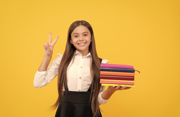 Chica adolescente feliz en uniforme escolar mantenga pila de libros mostrar educación de gesto de paz