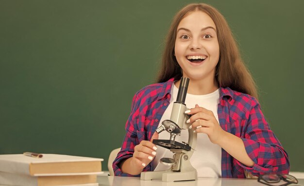 Chica adolescente feliz usando microscopio en la escuela secundaria en química de pizarra