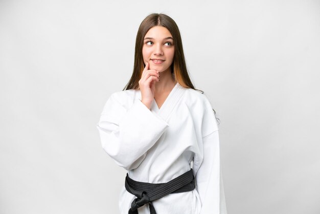 Chica adolescente haciendo karate sobre fondo blanco aislado pensando en una idea mientras mira hacia arriba