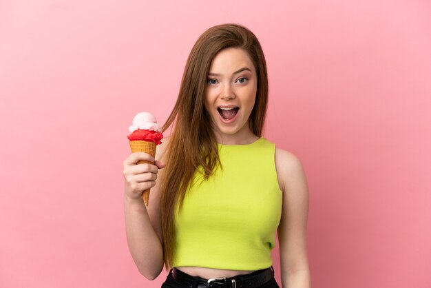 Chica adolescente con un helado de cucurucho sobre fondo rosa aislado con expresión facial sorpresa