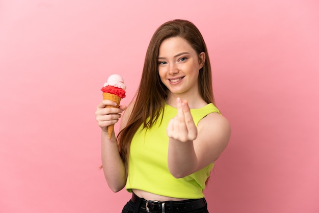 Chica adolescente con un helado de cucurucho sobre fondo rosa aislado haciendo gesto de dinero