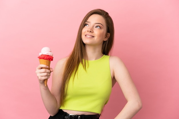 Chica adolescente con un helado de cucurucho sobre fondo rosa aislado pensando en una idea mientras mira hacia arriba