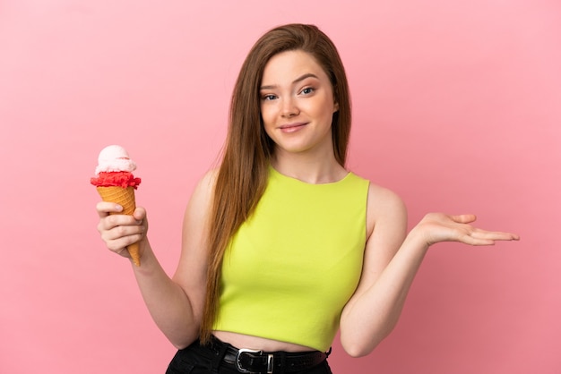Chica adolescente con un helado de cucurucho sobre fondo rosa aislado teniendo dudas mientras levanta las manos