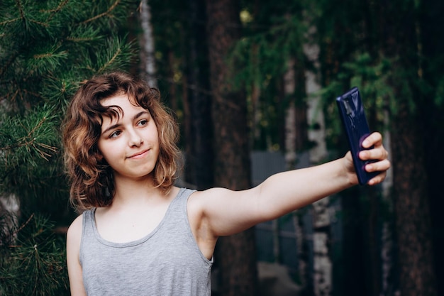 Chica adolescente hermosa tomando un selfie en el bosque. usando tecnología