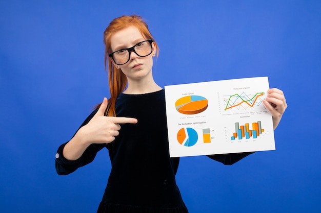 Foto chica adolescente inteligente con gafas y un vestido negro muestra estadísticas con gráficos circulares y gráficos azules